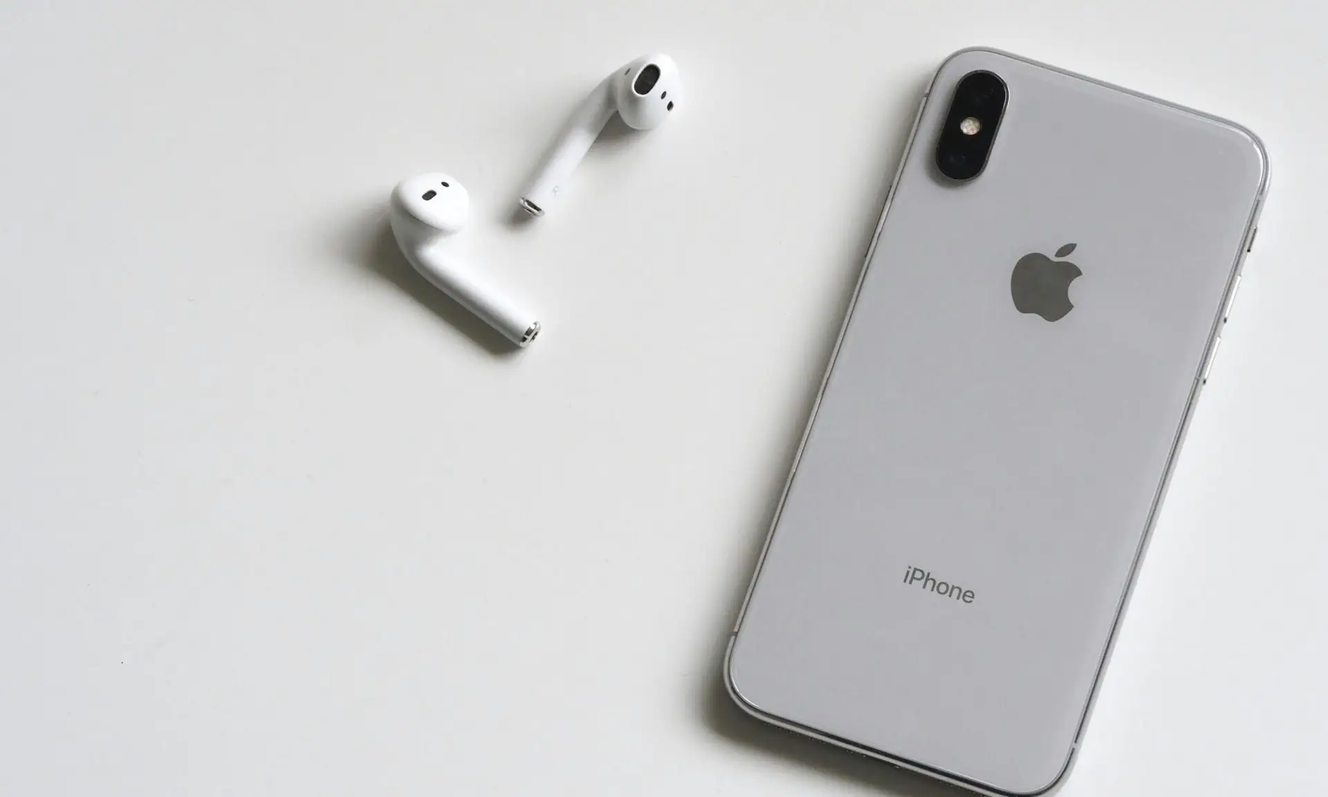Close-up of a silver iPhone and wireless AirPods on a sleek white background.